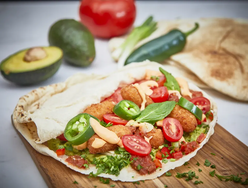 An open pita piled with falafel, tomato and peppers