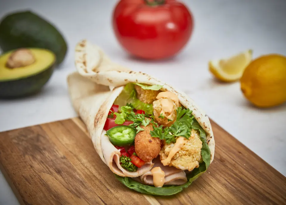 A pita rolled around chicken, peppers and sauce on a wooden board