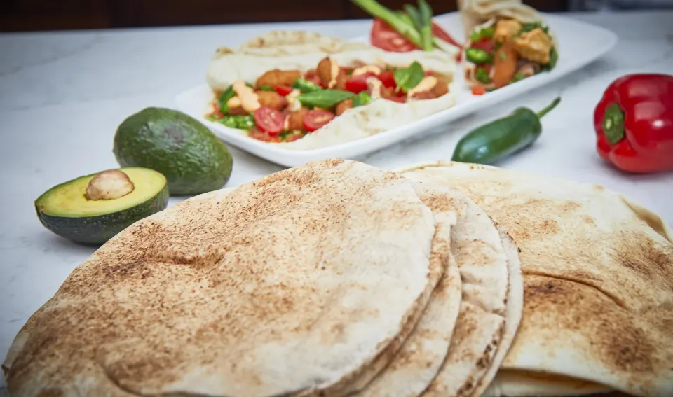 A stack of pocket pita with avocado, peppers and a filled pita behind