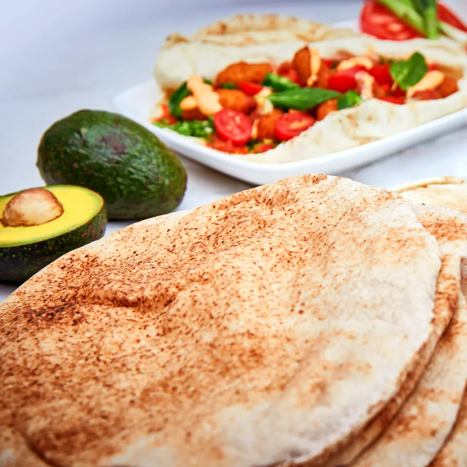 A stack of pocket pita, toasted in spots by the oven, beside a filled pita and avocado