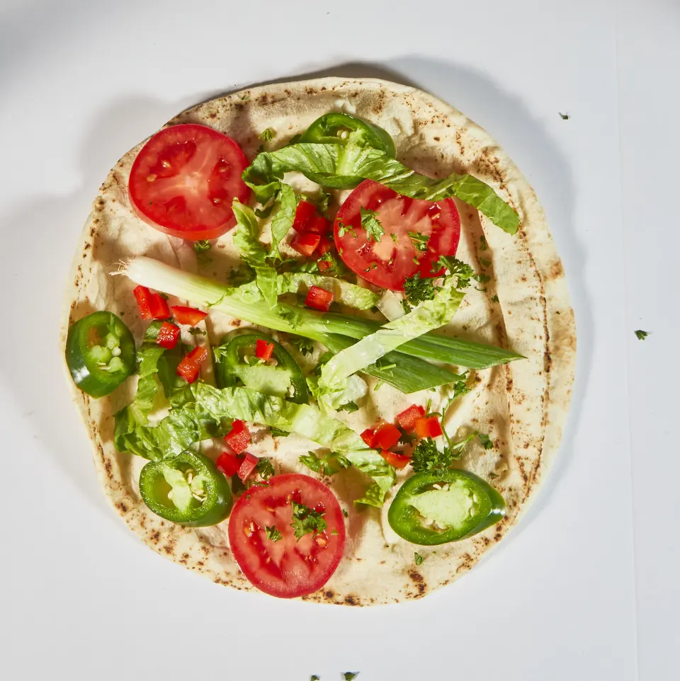 A pita pizza topped with tomato slices and green peppers